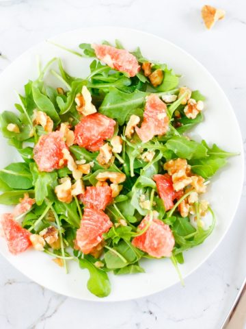 Overhead view of a plate of grapefruit arugula salad on a marble table with a fork on the side.