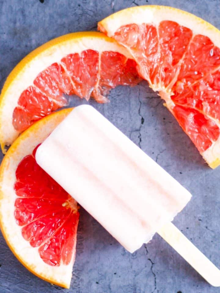 grapefruit popsicles lying on top of three slices of fresh grapefruit
