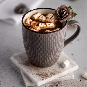 Healthier hot chocolate, topped with mini marshmallows, in a grey mug on a stack of two white marble coasters.