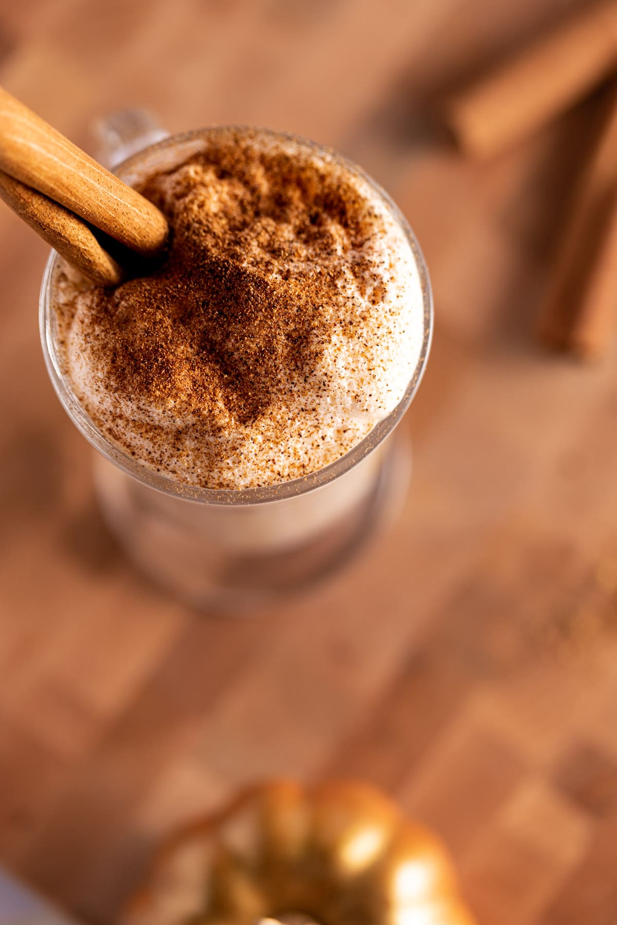 Overhead photo of an iced latte with pumpkin foam on top, on a wooden board, with golden decorative pumpkins around the glass.