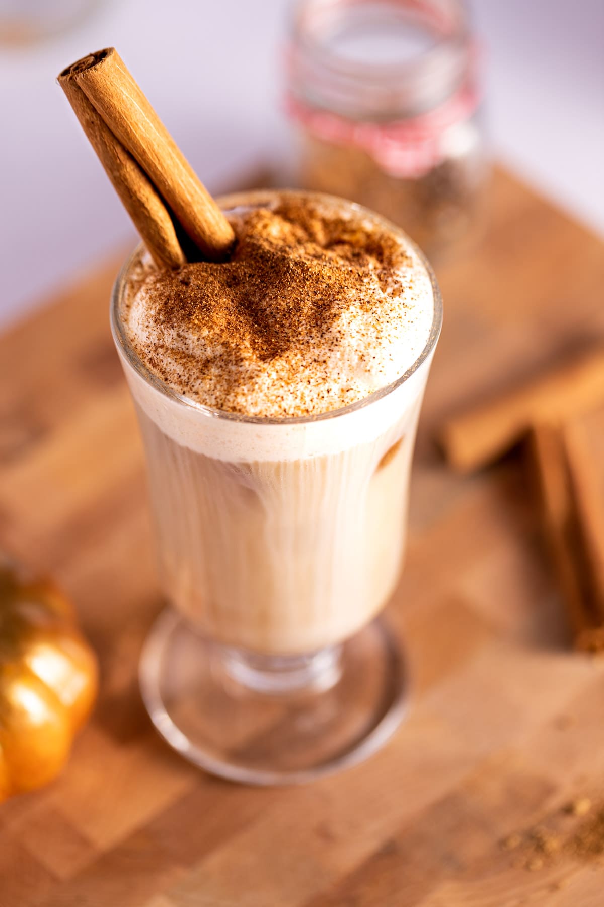 Overhead shot of a chai latte topped with pumpkin cold foam and sprinkled with cinnamon, with a cinnamon stick as garnish.
