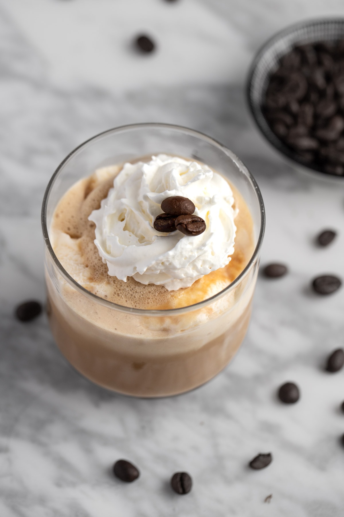 Iced coffee with ice cream topped with whipped cream and coffee beans, on a marble table.