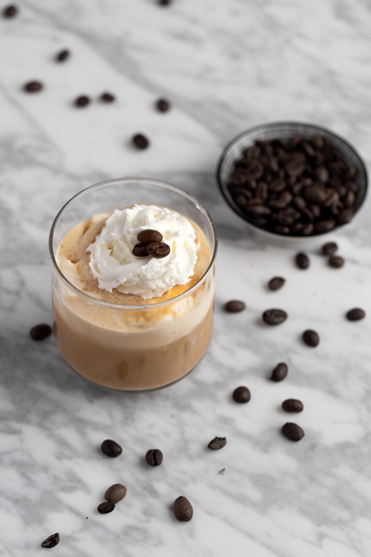 Coffee with ice cream in a glass, on a marble table next to scattered coffee beans.