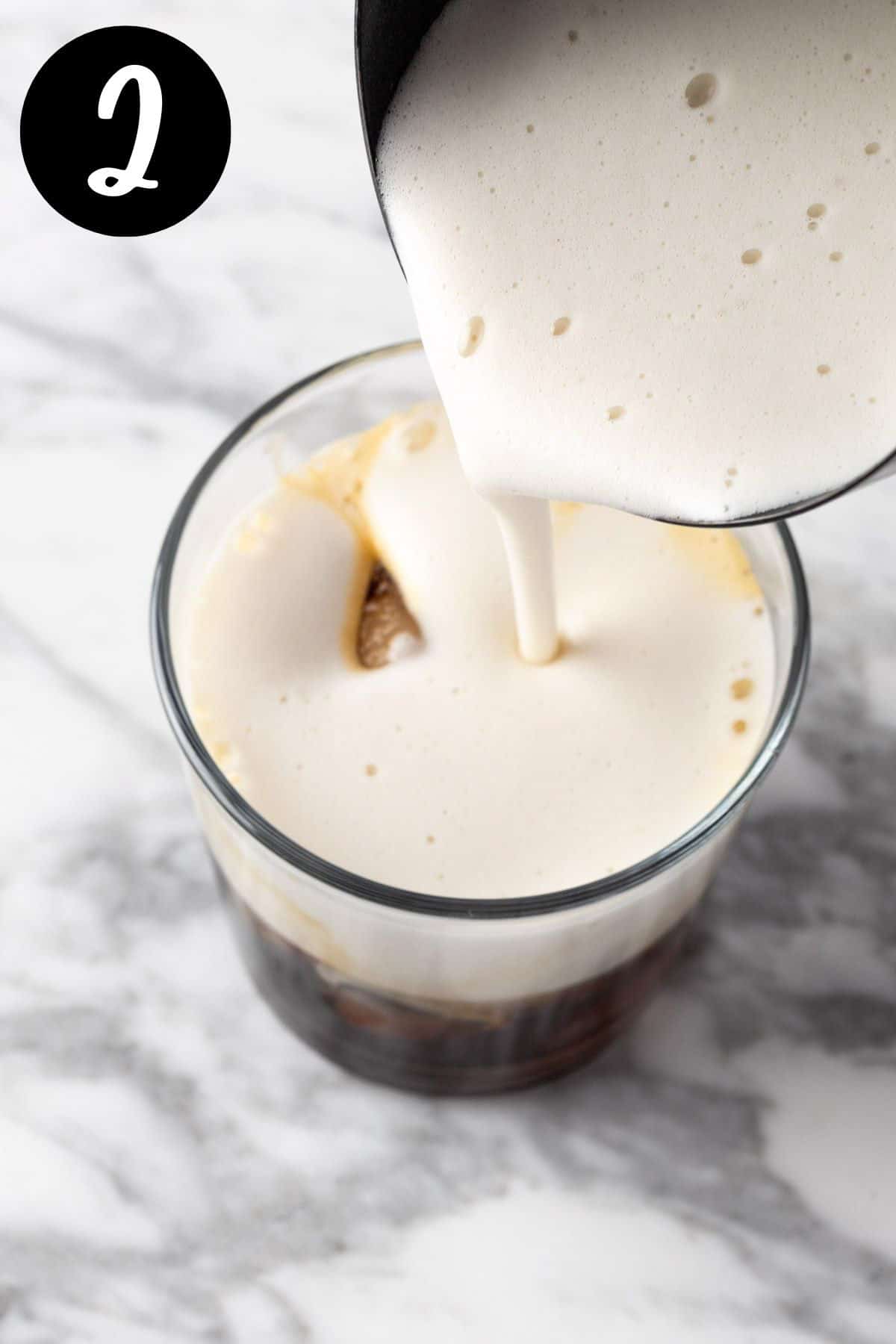 Pouring the frothed gingerbread milk on top of the chilled espresso.