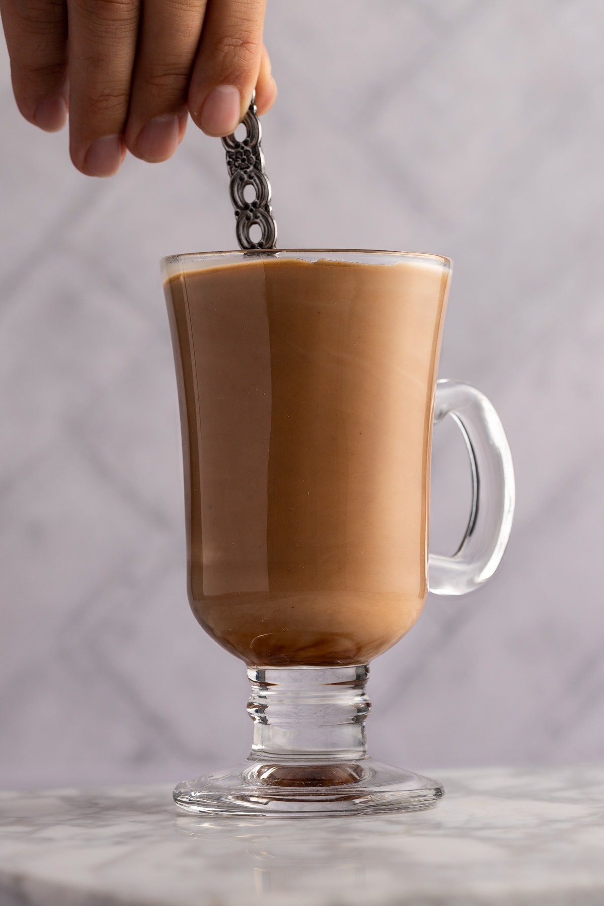 A hand using a spoon to stir the mocha latte ingredients together, with a white background.