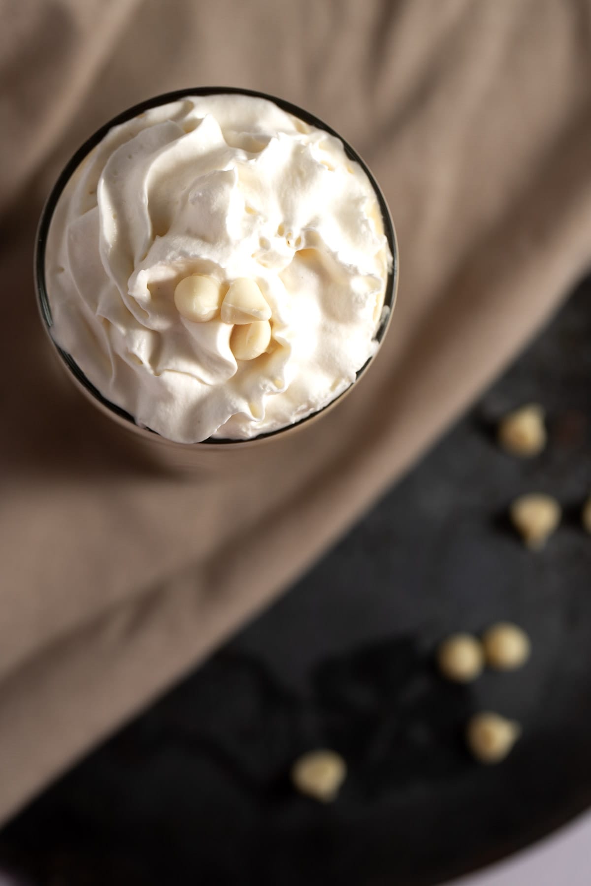 Overhead view of an iced latte, topped with whipped cream, sitting on a black metal plate, next to a brown napkin.