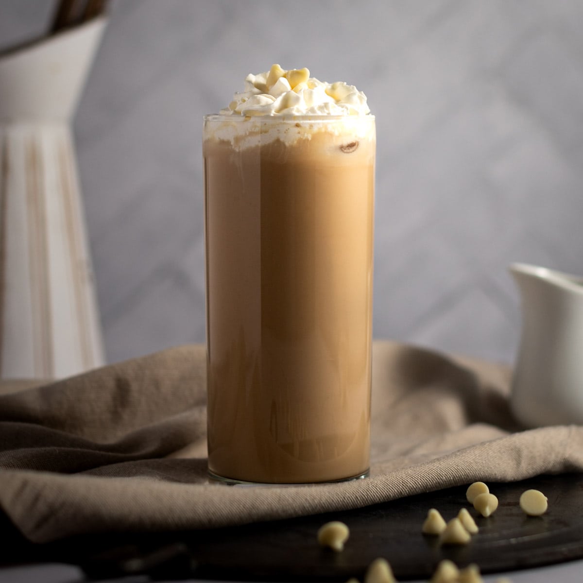 An iced white chocolate mocha in a tall glass, topped with whipped cream and white chocolate chips. 