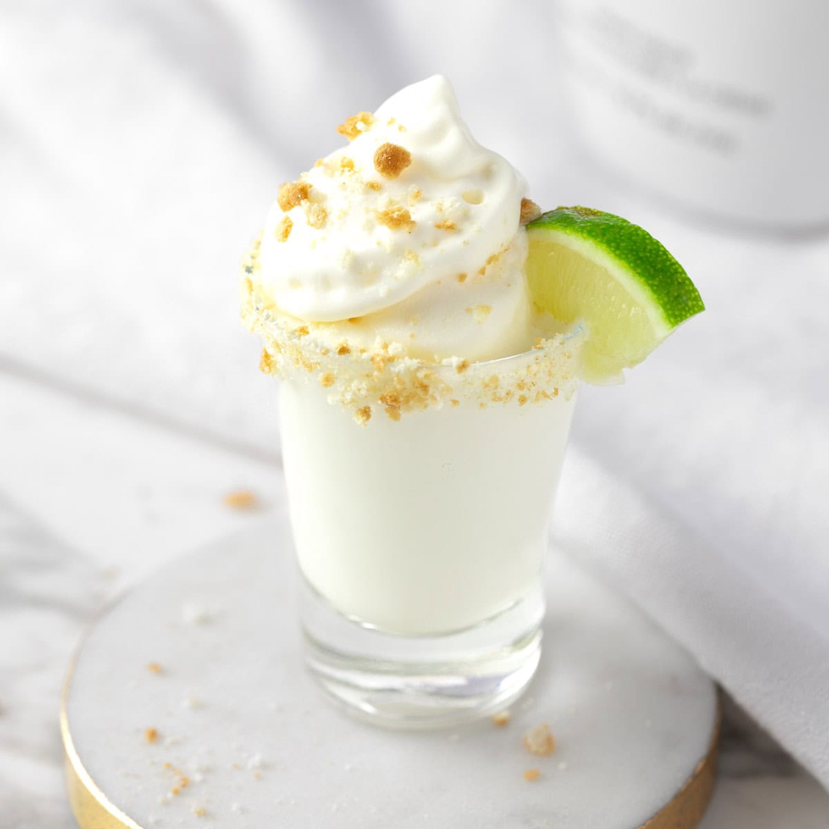 A key lime pie shot topped with whipped cream and graham cracker crumbs.