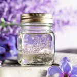 Lavender syrup in a small jar, with purple lavender flowers in the background.