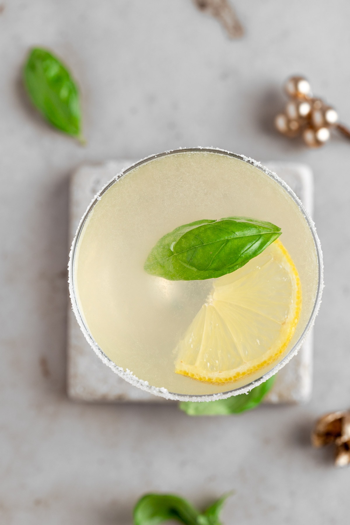 Overhead view of a lemon basil martini garnished with a basil leave and a lemon wedge.