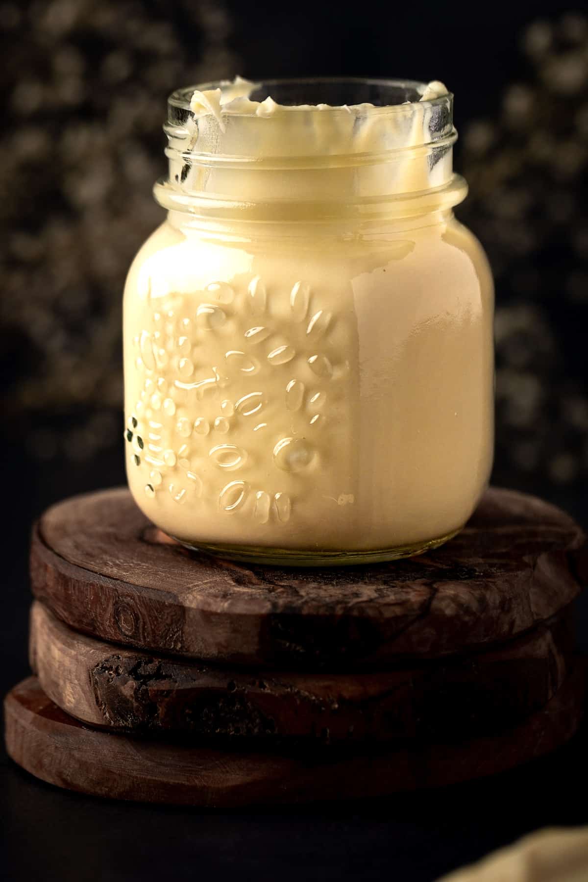 A small jar of lemon ganache on 3 stacked wooden coasters.