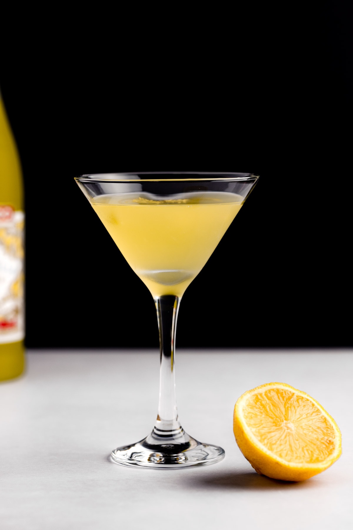 Eye level view of a limoncello martini, on a white table with a black background.