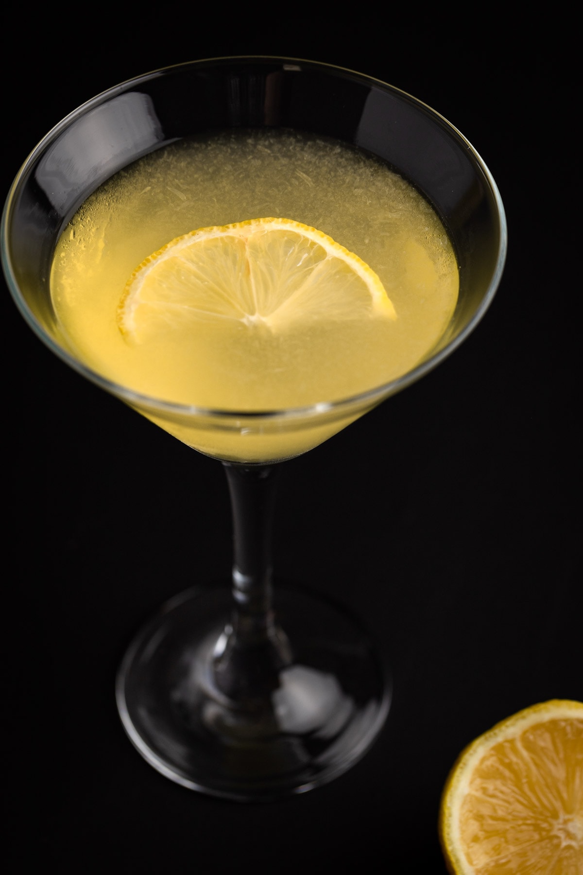 Overhead view of a limoncello martini garnished with a lime slice, on a black background.