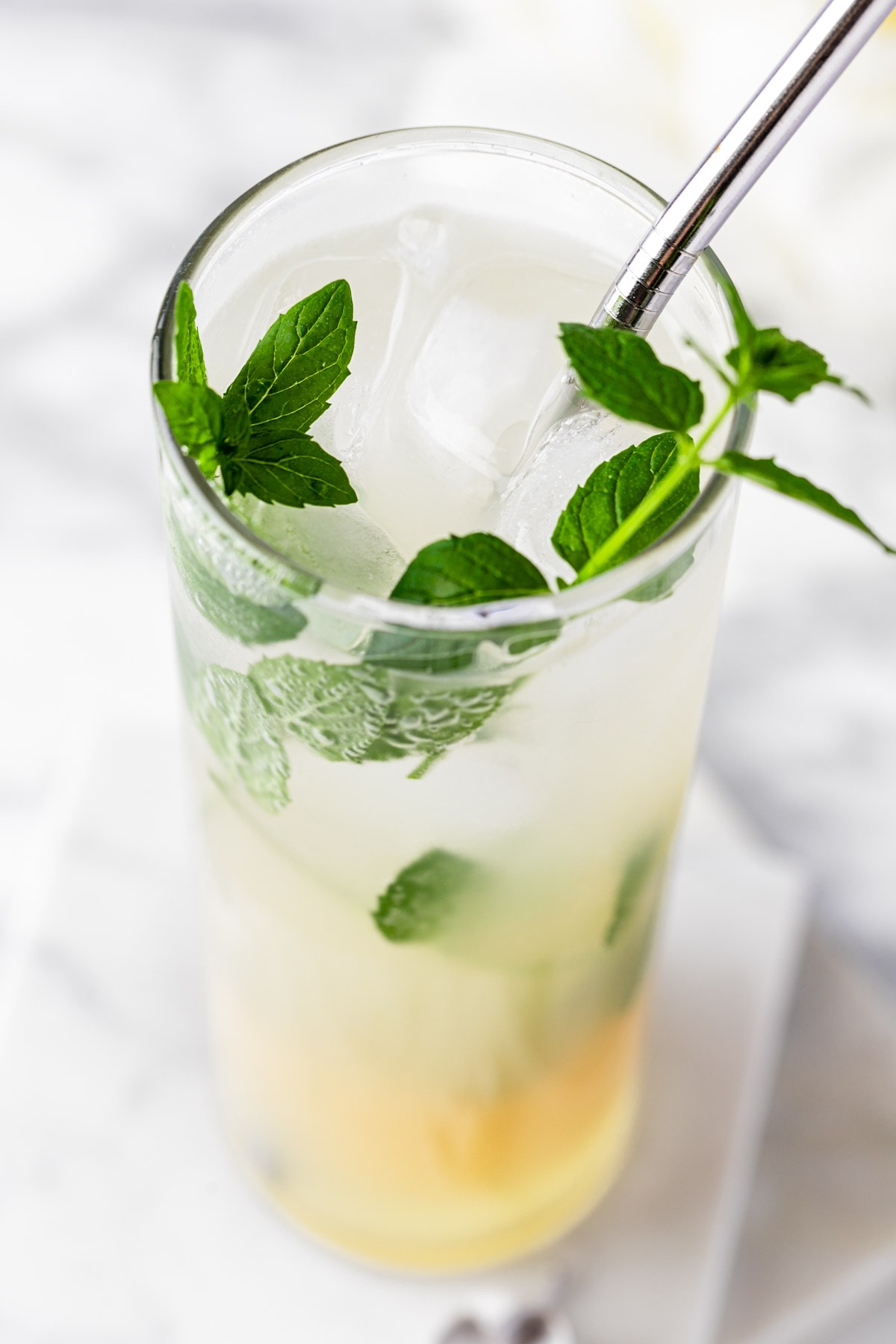 A lychee mojito garnished with fresh mint, on a white marble table.