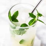 A lychee mojito garnished with fresh mint, on a white marble table.