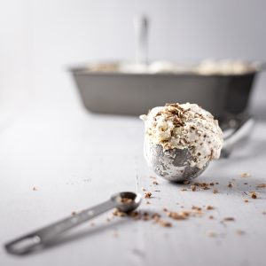 An ice cream scoop of macadamia ice cream with toasted coconut on top, and a measuring spoon in the foreground