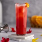 A red madras drink in a tall glass, garnished with an orange peel twist.