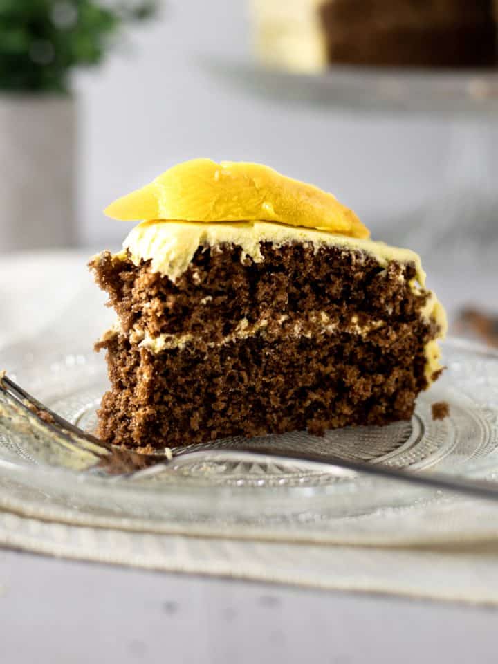 Piece of mango chocolate cake with a fresh mango slice on top, on a glass plate on a beige napkin