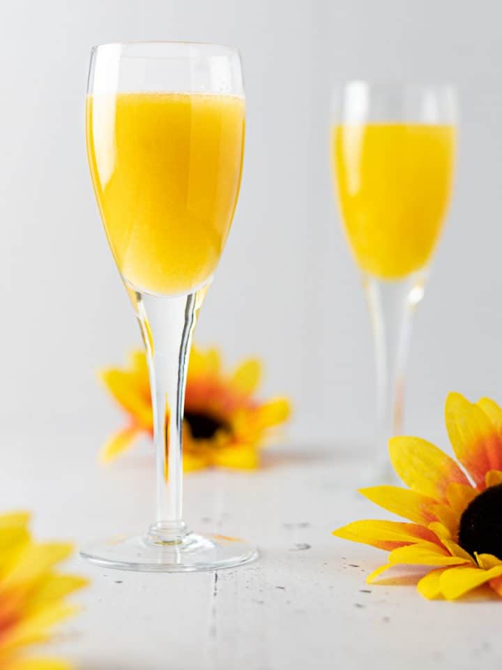 Two glasses of mango gin cocktail with three sunflowers scattered around them.