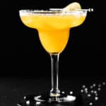 A mango margarita on the rocks with a salted rim, on a black background.