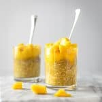 Side angle view of two jars of overnight oats with mango pieces scattered around beside them