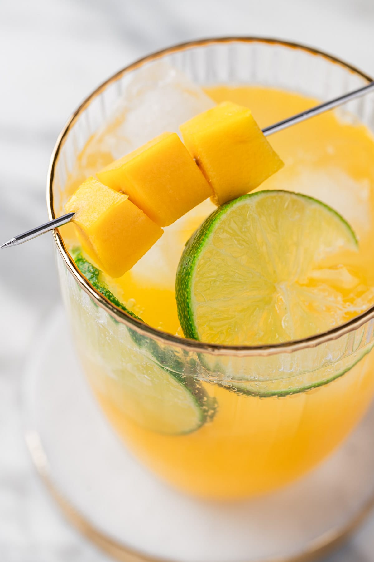 A mango rum cocktail garnished with fresh mango chunks and lime slices.