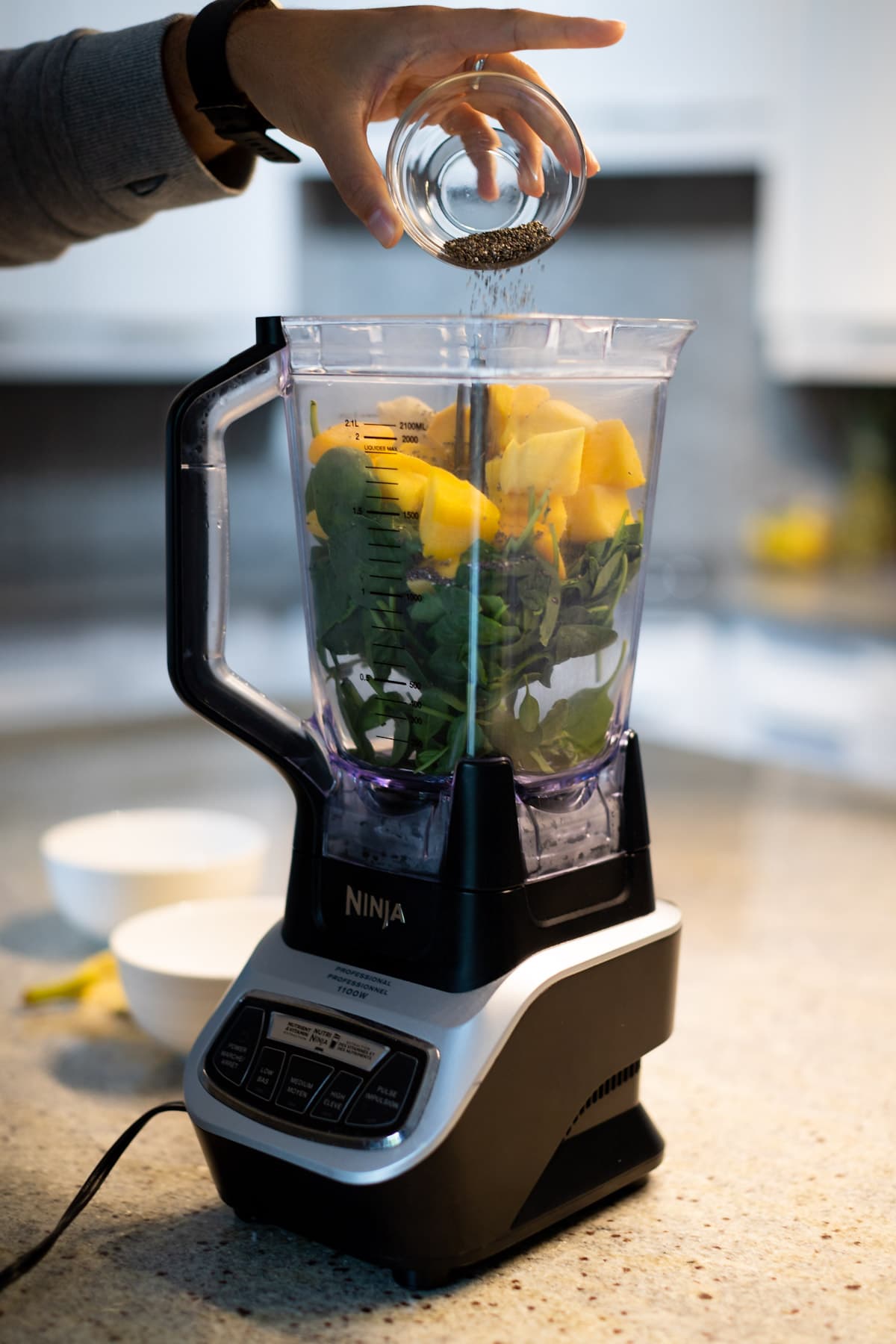 Chia seeds being poured into a blender with the rest of the smoothie ingredients.