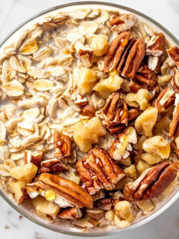 A bowl of maple brown sugar overnight oats topped with toasted nuts and a drizzle of maple syrup.