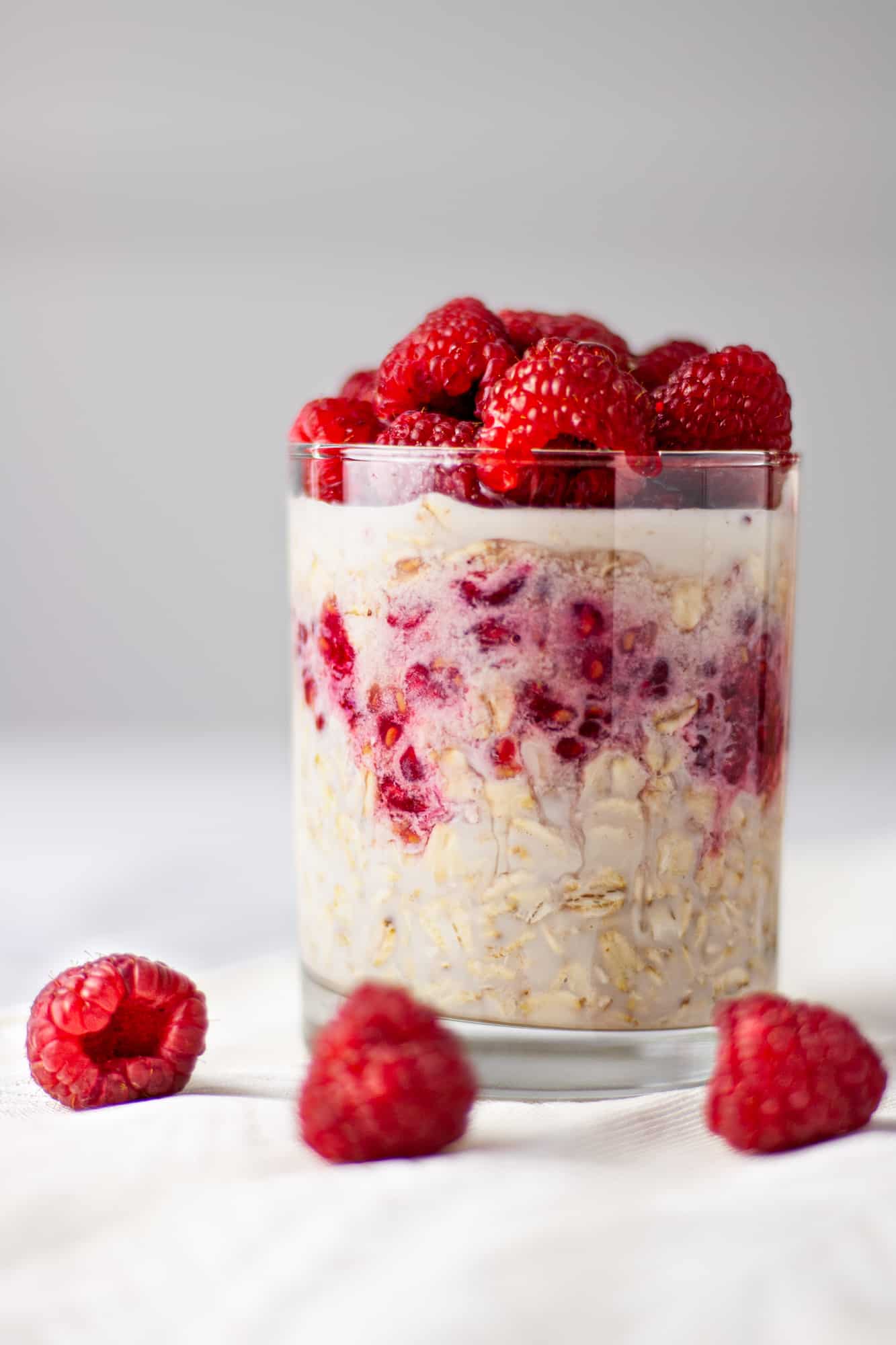 Up close side angle view of overnight oats with three raspberries sitting in front of the glass