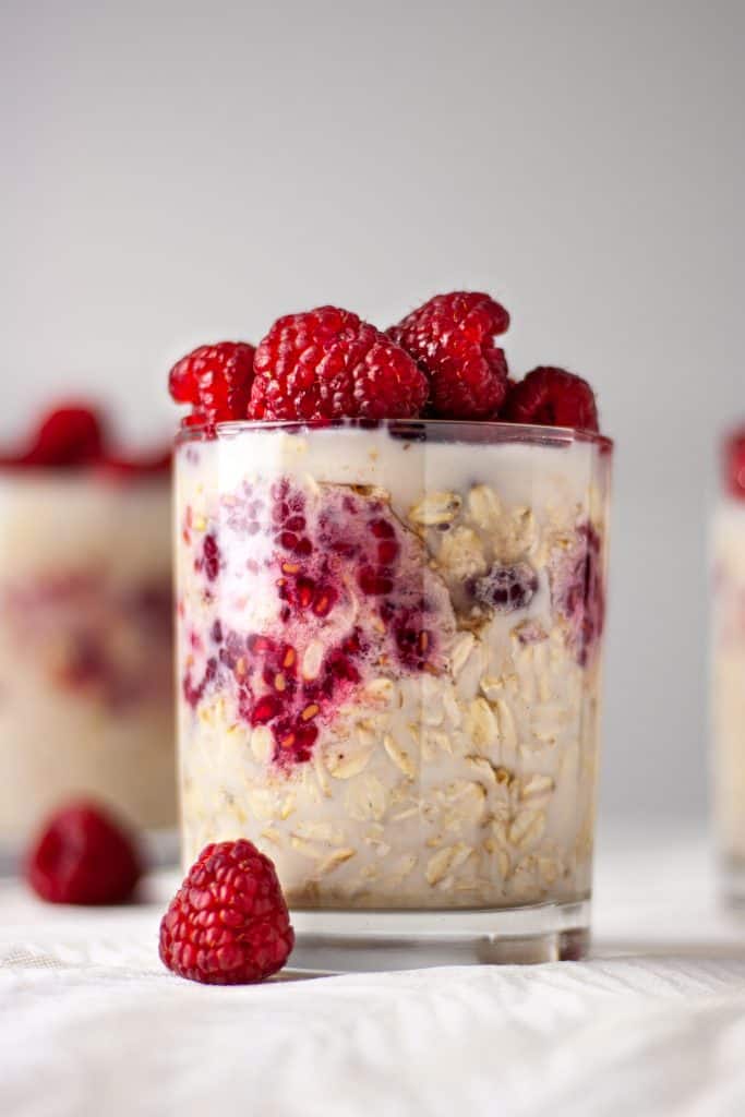 Side angle view of a glass of maple raspberry overnight oats topped with fresh raspberries