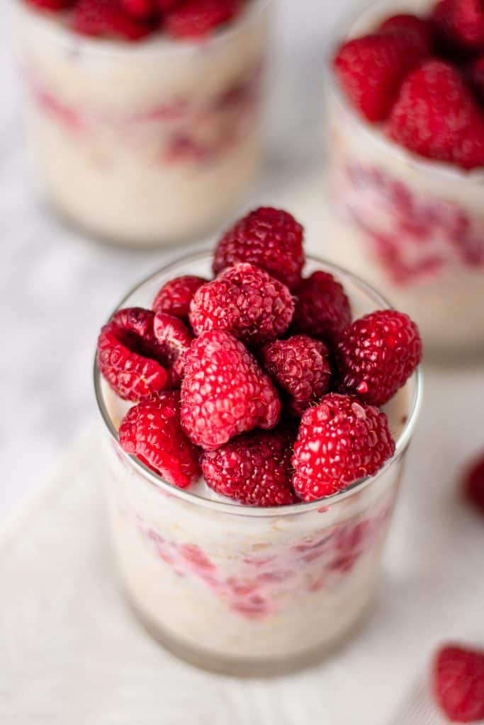 Overhead view of fresh raspberries on top of a glass of maple raspberry overnight oats