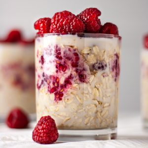 Side angle view of a glass of maple raspberry overnight oats topped with fresh raspberries