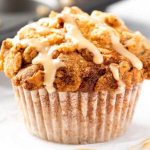 A maple walnut muffin drizzled with maple glaze, sitting on white marble table.