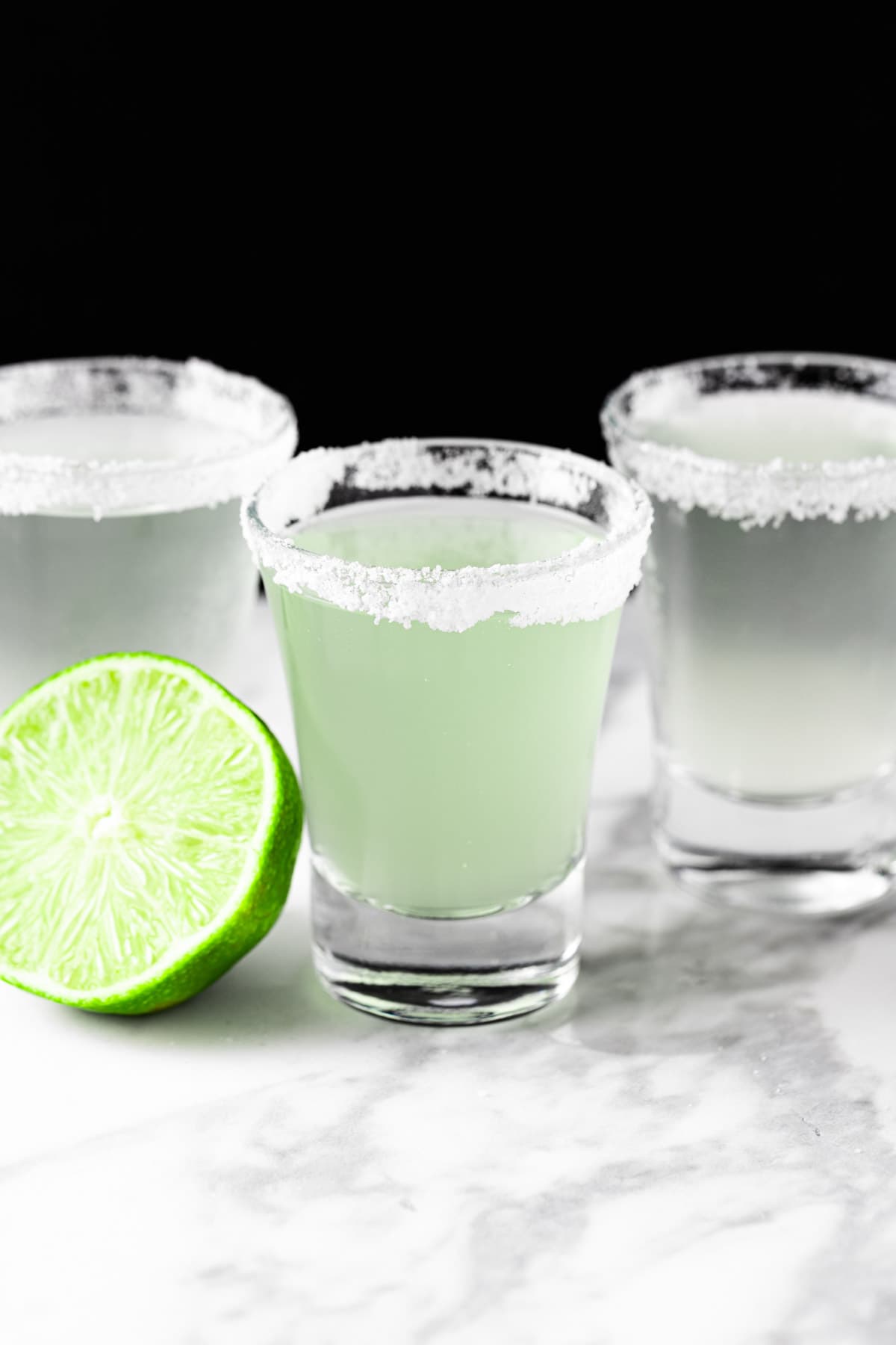 Three margarita shooters on a white marble table.