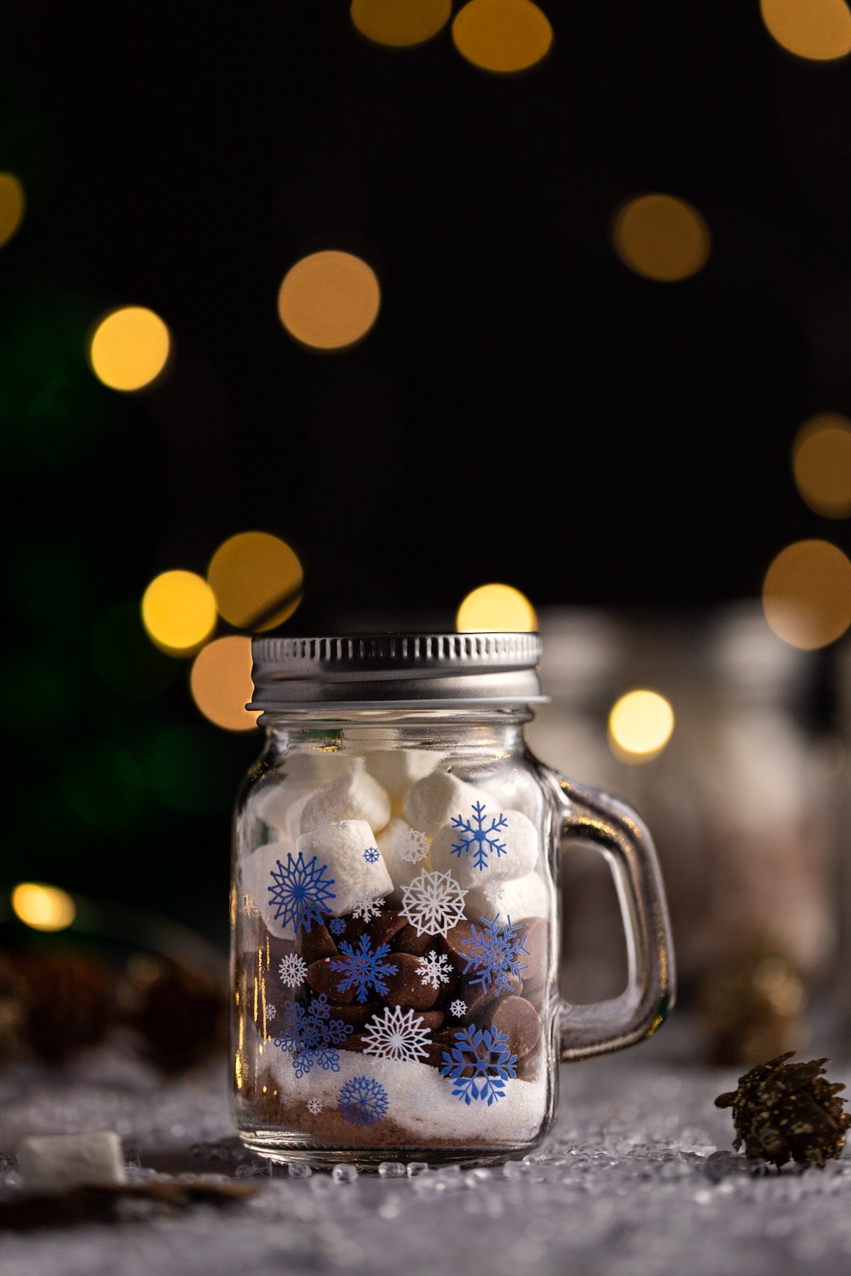 Mason jar hot chocolate with sugar, chocolate chips and marshmallows, christmas lights on a black background.