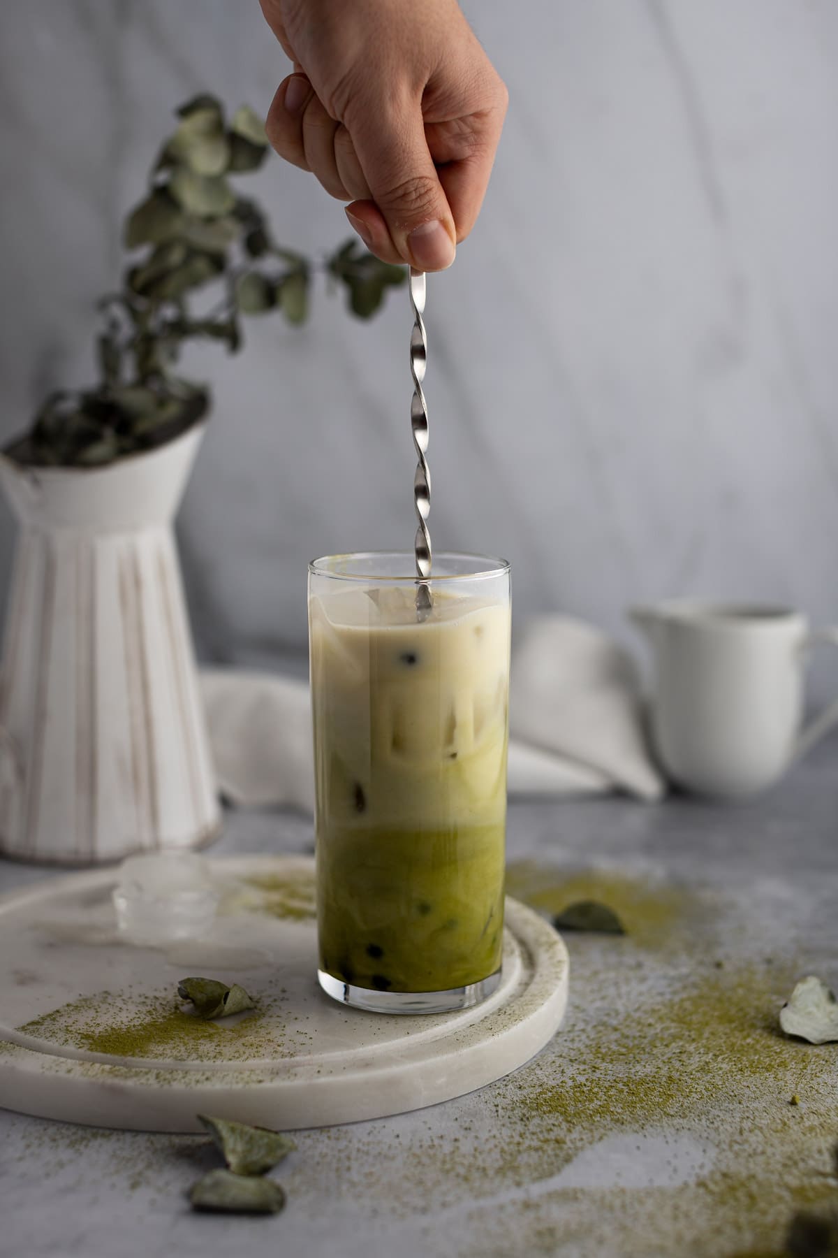 A hand holding a long metal spoon and stirring the almond milk into the matcha boba tea.