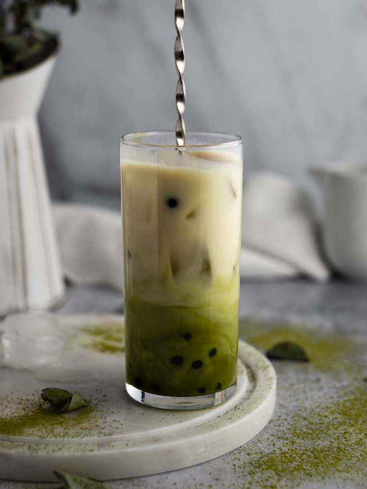 A spoon stirring the matcha milk tea to mix the green matcha and white almond milk together.