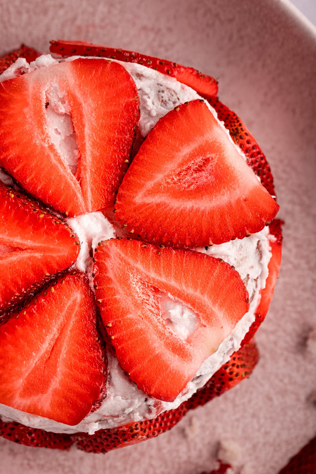 An overhead view of a round small strawberry cake topped with slices of strawberry.