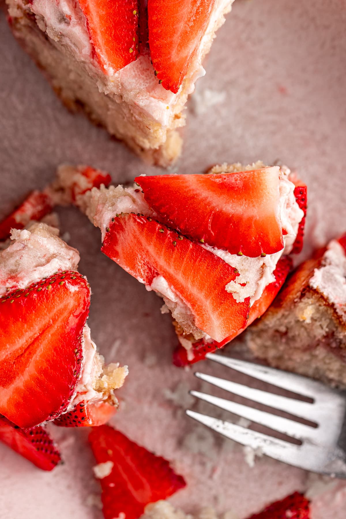 A slice of a mini strawberry cake topped with strawberry frosting and decorated with slices of fresh strawberries.