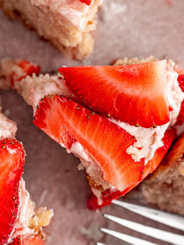 A slice of a mini strawberry cake topped with strawberry frosting and decorated with slices of fresh strawberries.