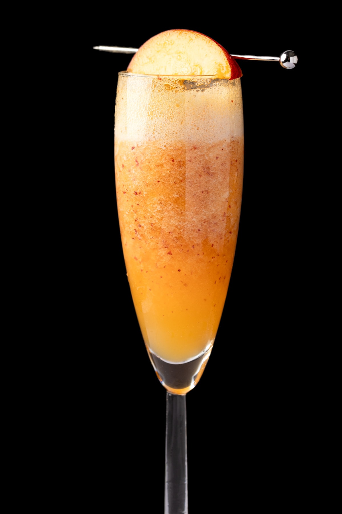 A non alcoholic peach bellini garnished with a slice of fresh peach, on a black background.