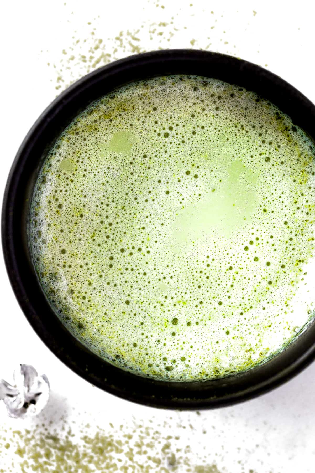 Overhead view of a frothy oat milk matcha latte in a black mug.