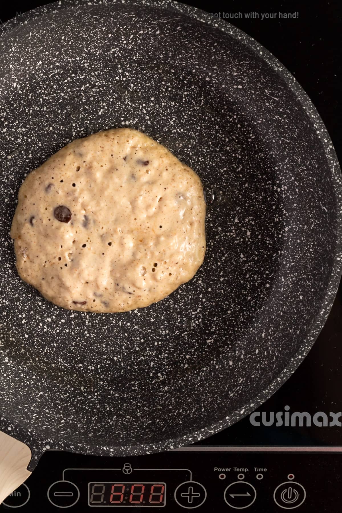 Overhead view of a pancaked being cooked on a the stovetop on a speckled grey pan.