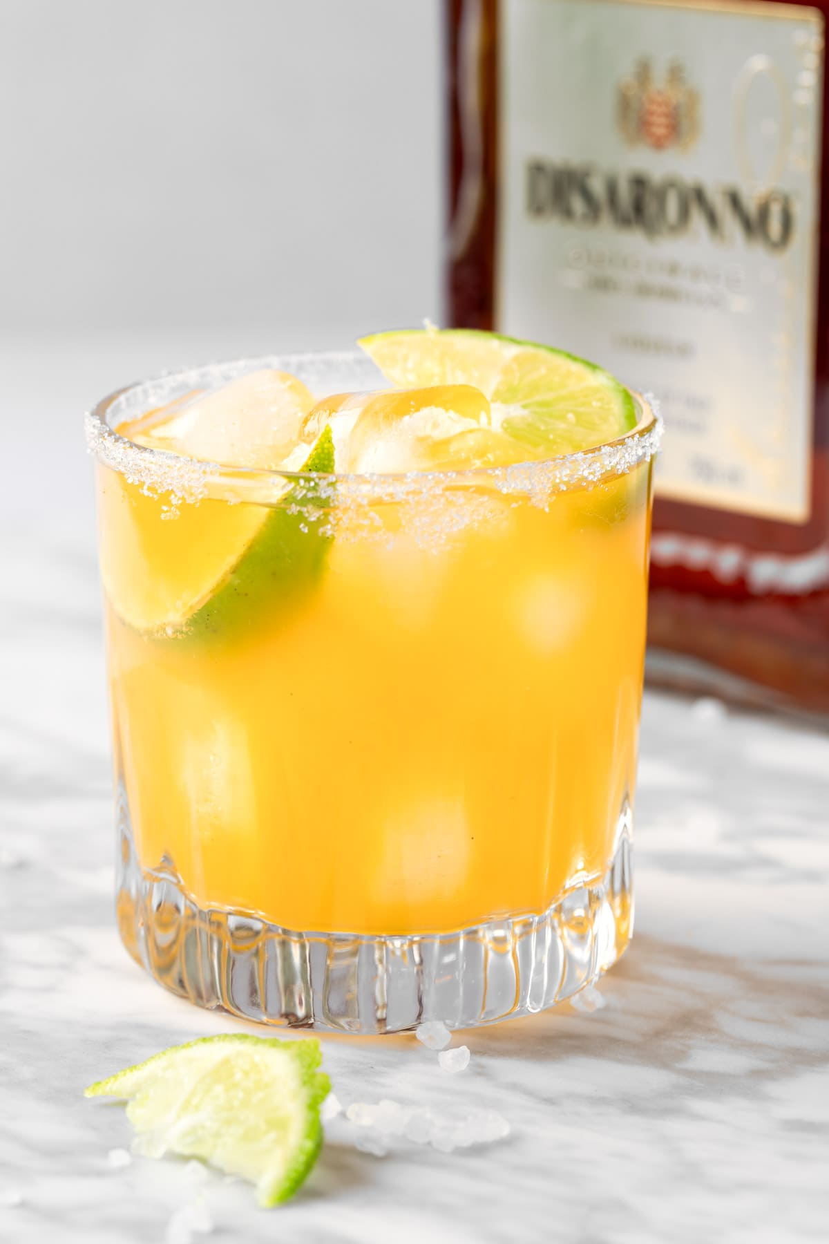 An Olive Garden Italian Margarita garnished with lime, with an amaretto bottle in the background.