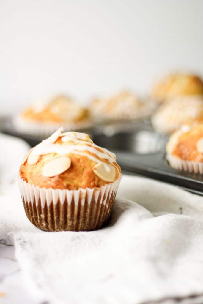 An orange almond muffin on a white hand towel with a full muffin tray in the background