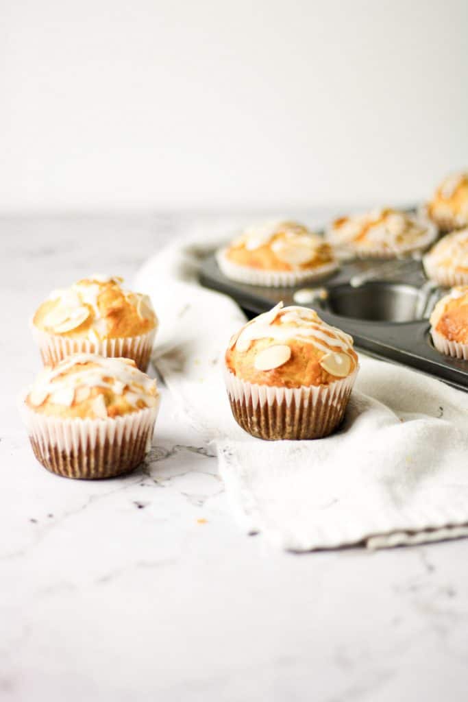 Three orange almond muffins with orange glaze on the table next to a muffin tray
