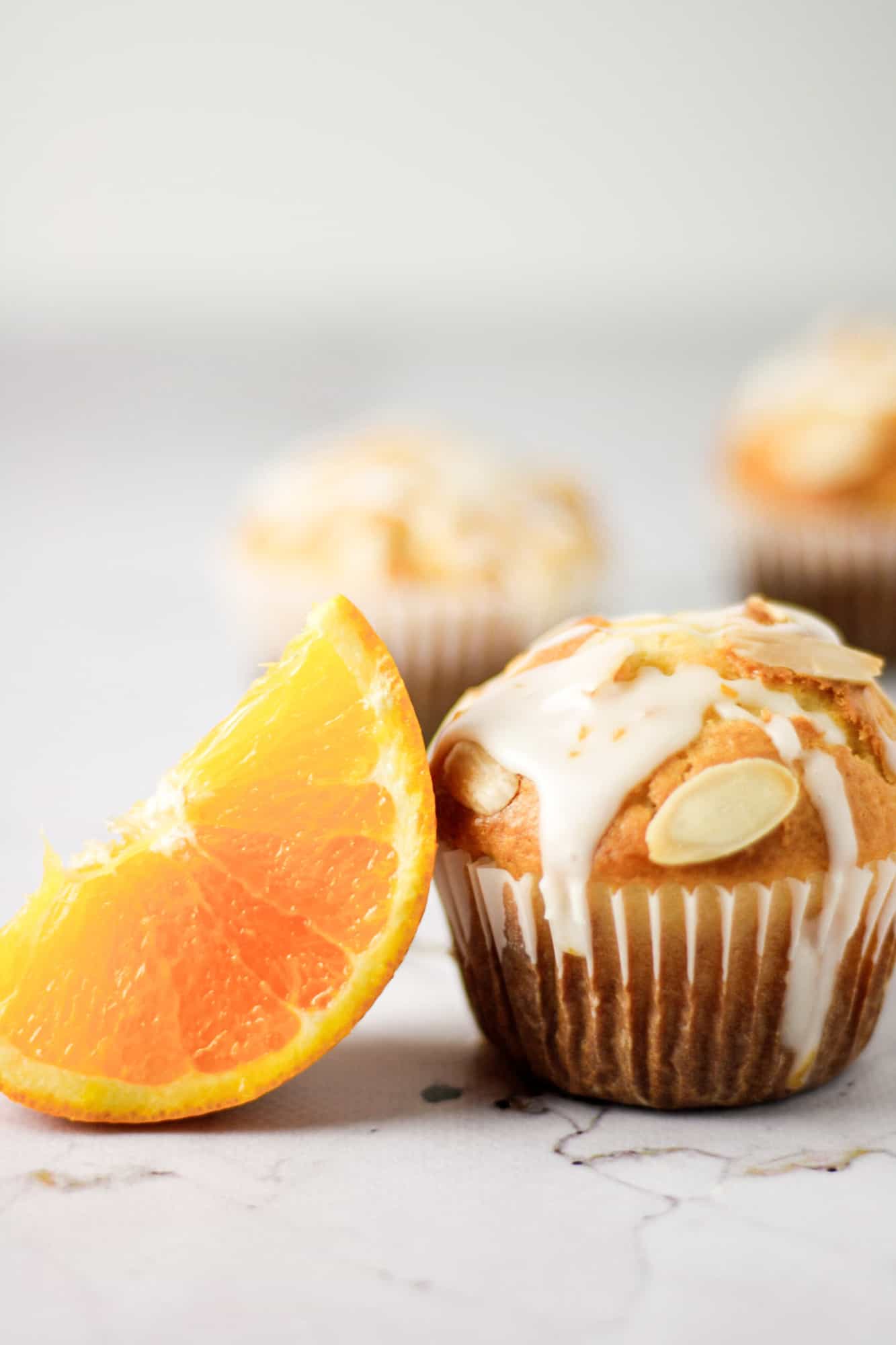 An orange slice leaning on a single orange almond muffin with orange glaze