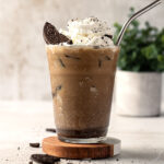 A glass of Oreo iced coffee topped with whipped cream and Oreo pieces.