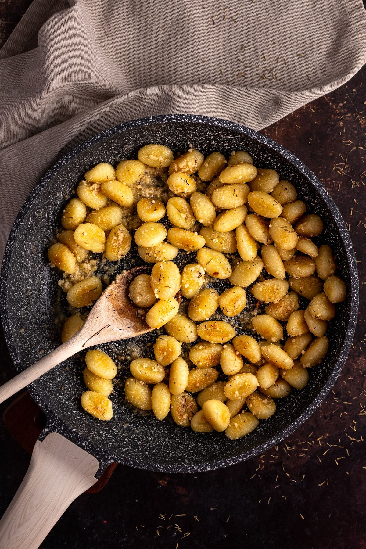 Overhead view of a pan filled with fried gnocchi, on a dark brown table.