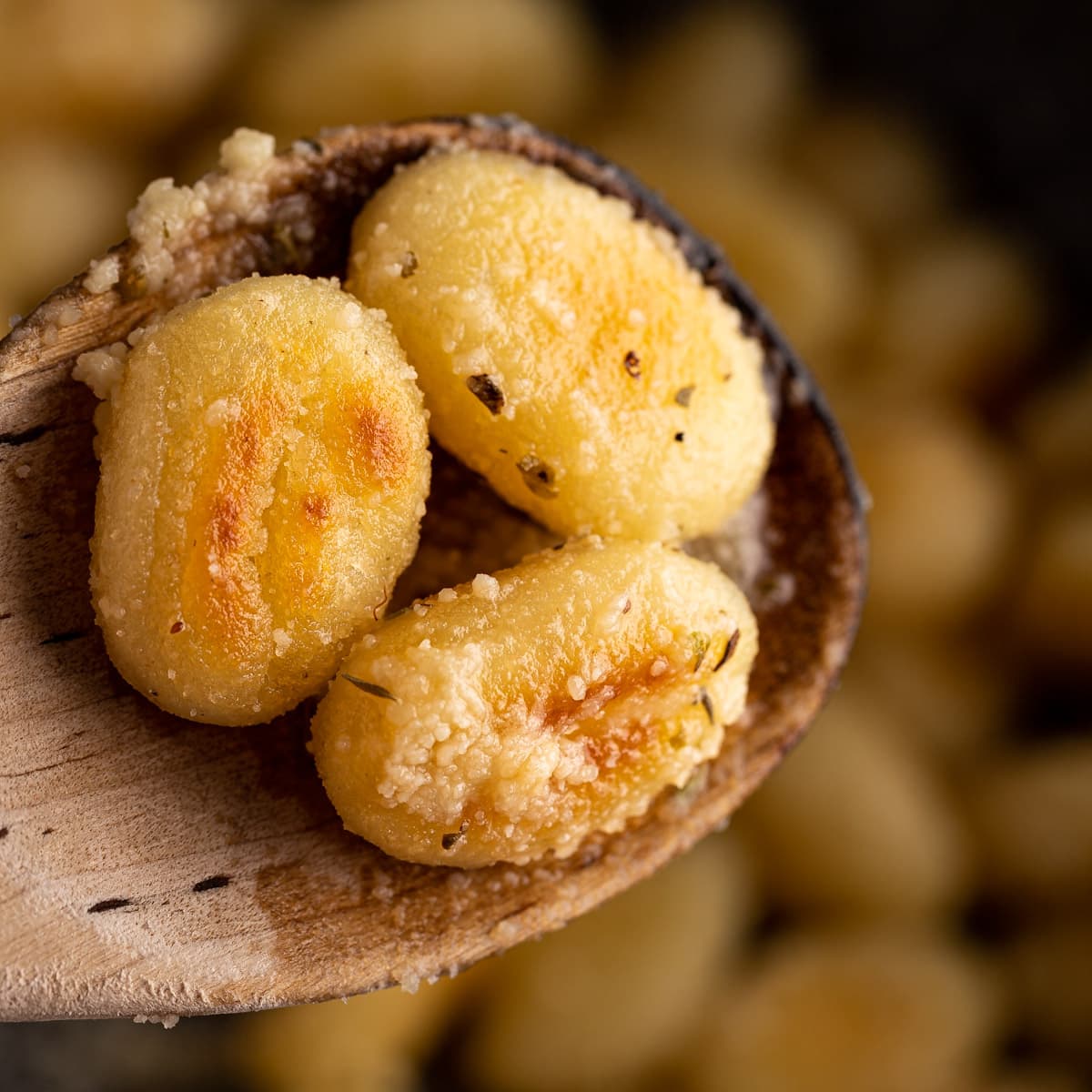 Up close view of 3 pan fried gnocchi pieces on a wooden spoon. 